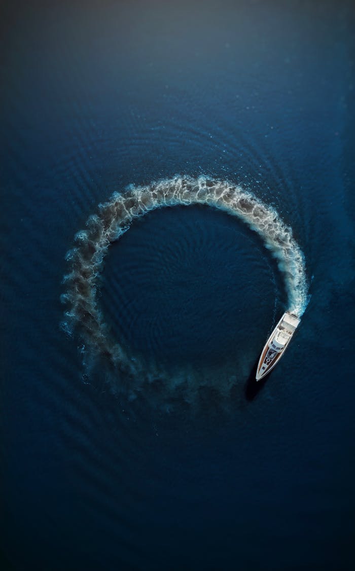 An aerial shot of a motorboat making a circular ripple pattern in the azure ocean water, showcasing motion and summer vibes.